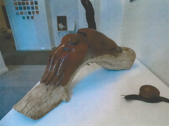 A photograph of two sculptures at an exhibition. A giant cuttlefish rests on a branch and a sea snail moves beside it.