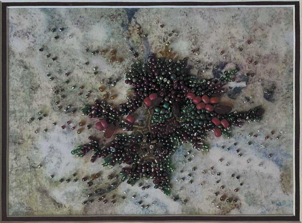 A framed picture of red, green, blue and gold beads forming a shape like seaweed on a rock.