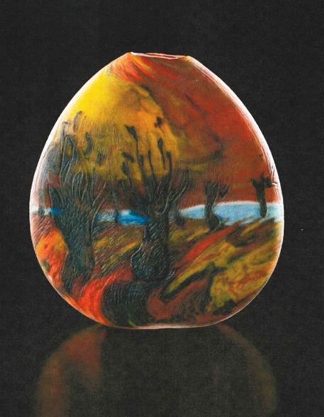 An egg-shaped glass vase boldly colored yellow and red with foliage around a waterhole.